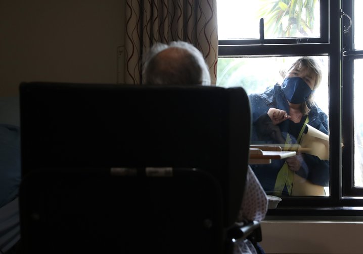 An elderly resident talks to a visitor through the window at nursing home in south London